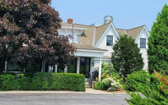 Exterior of Two-story white clapboard New England Inn behind artfully landscaped front foliage.